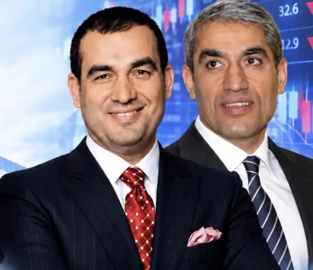 Koyu takım elbiseli iki iş insanı yan yana poz veriyor; arkada borsa grafikleri görünüyor